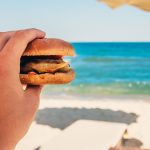 Holding a burger by the sea before going for a swim