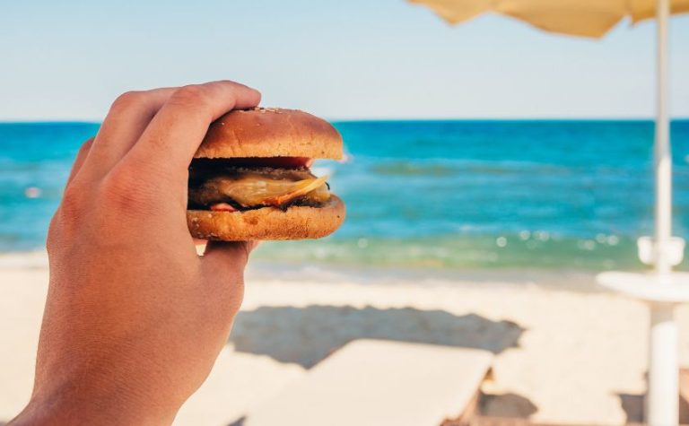Holding a burger by the sea before going for a swim
