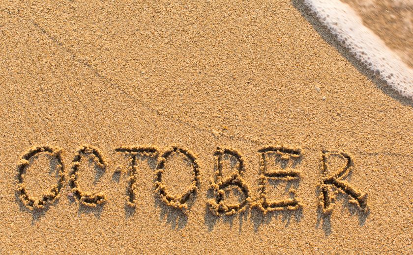 The word “October” written in sand, symbolizing autumn in Zakynthos by the beach.